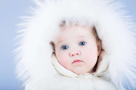 Sweet baby in a white snow suit with a fur hood looking tired の写真素材