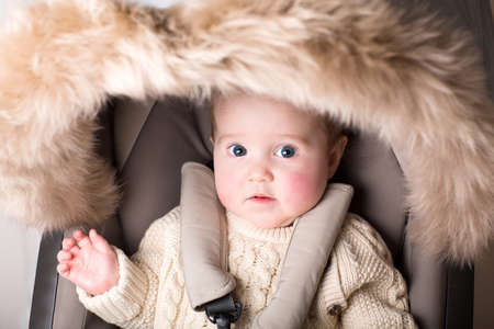 Sweet baby with big beautiful eyes sitting in a luxury fur stroller の写真素材