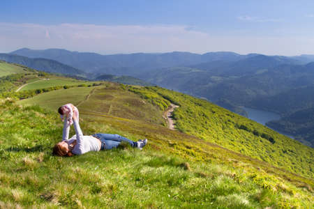 Young mother and her newborn baby relaxing high in the mountains with a stunning view over a lake の写真素材