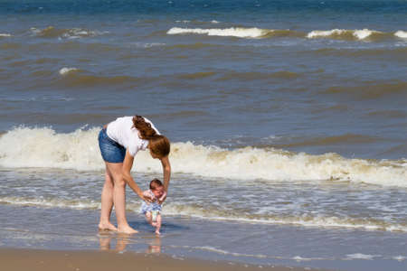 Young mother and her newborn daughter for the first time on a beach の写真素材