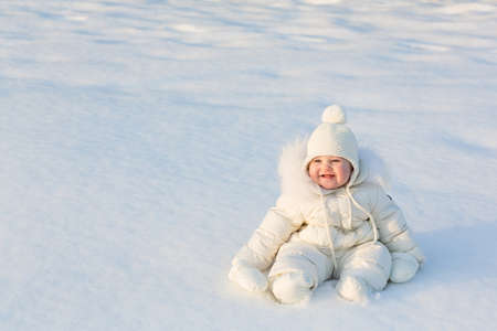 Beautiful baby in a white snow suit sitting on fresh snow on a sunny winter day の写真素材
