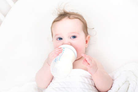 Little baby drinking milk from a bottle in a white crib の写真素材
