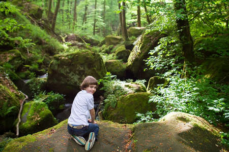 Cute boy playing on the rocks near a scenic waterfall の写真素材