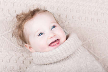 Cute funny baby girl in a knitted sweater on a knitted blanket の写真素材