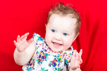 Cute laughing baby girl in a summer dress on a red blanket 