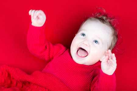 Laughing playing baby girl under a red blanket の写真素材