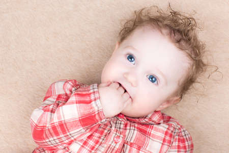 Funny baby girl in a red plaid shirt sucking on her finger 