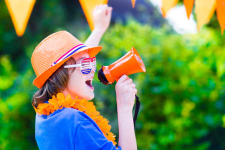 Happy Dutch boy, football fan, cheering and supporting soccer team of Netherlands during...
