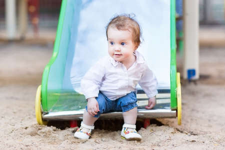Sweet baby girl with beautiful blue eyes playing on a slide の写真素材
