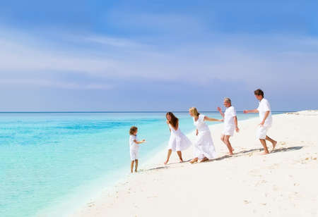 Happy family with grandparents, young couple and child playing on a beach 