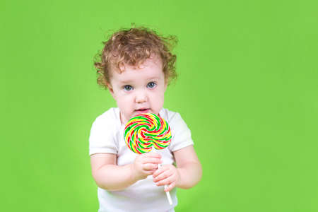 Funny curly baby with a colorful candy on green background の写真素材