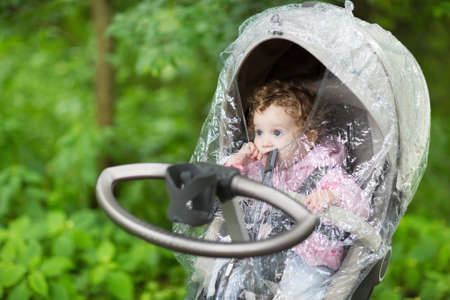 Little baby girl sitting in a stroller under a rain cover on a cold and rainy autumn day の写真素材