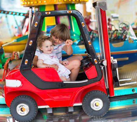 Brother and little baby sister enjoying a ride in an amusement park の写真素材