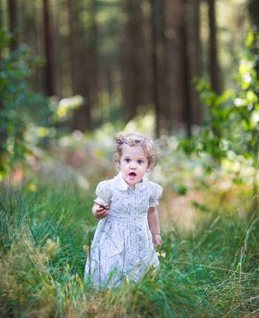 Beautiful little girl wearing a white dress walking in a sunny autumn park の写真素材