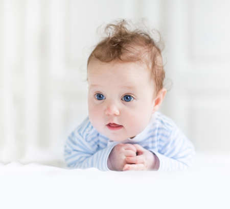 Funny baby girl with beautiful blue eyes playing on her tummy in a white nursery の写真素材