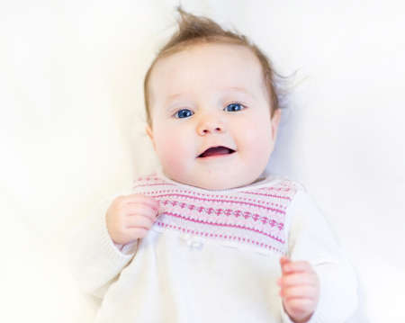 Beautiful baby girl in a warm knitted pink dress on a white blanket 