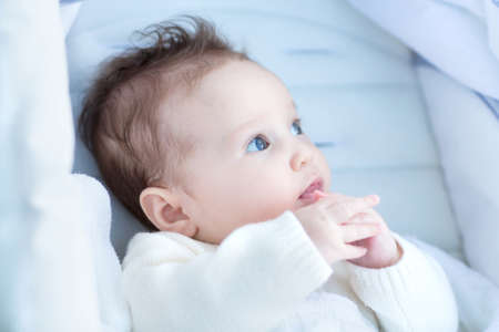 Beautiful little baby relaxing in a stroller wearing a warm white knitted sweater の写真素材