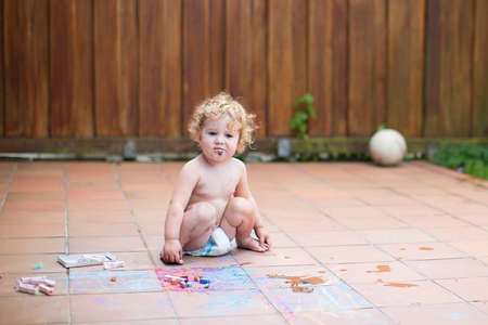 Funny little baby girl wearing a diaper painting with chalk in the back yard of a house の写真素材