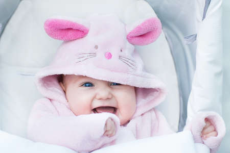 Adorable funny baby girl sitting in a stroller in a bunny snow suit on a walk in a cold winter park の写真素材