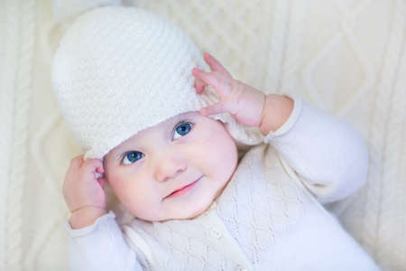 Beautiful baby girl wearing knitted sweater and hat relaxing on a warm blanket の写真素材