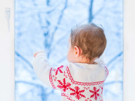 Sweet baby watching ot out a window to a snowy garden on Christmas day の写真素材