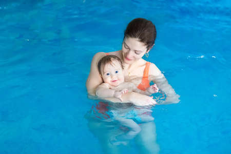 Young mother and her baby enjoying a baby swimming lesson in the pool の写真素材
