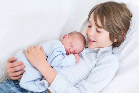 Happy laughing boy holding his sleeping newborn baby brother の写真素材