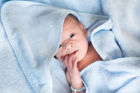 Newborn baby relaxing after a bath in a blue towel の写真素材
