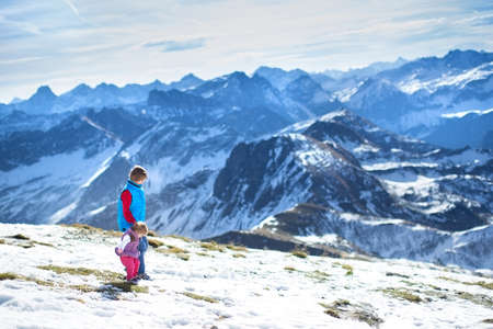 Happy boy playing with his little baby sister in the snow next to beautiful mountains の写真素材