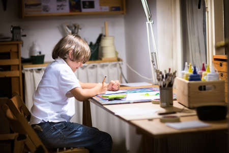 Little boy painting in a dark room late in the evening の写真素材