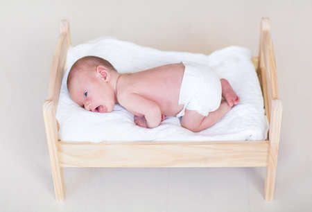 Adorable tiny newborn baby in a wooden toy bed の写真素材