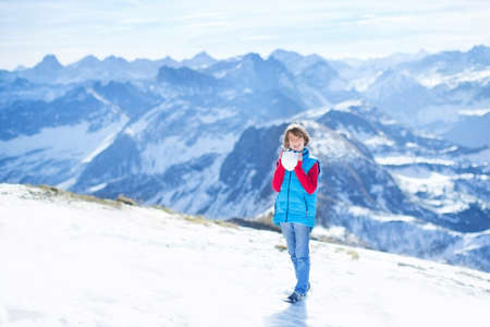 Happy little boy playing snow ball fight in the beautiful snow covered Alps mountains の写真素材