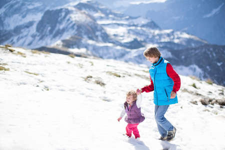 Two children, a teenager boy and his little sister, playing together in snow in the mountains の写真素材