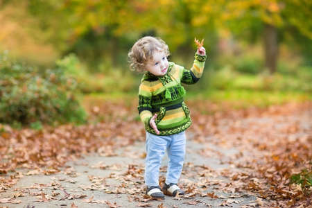 Sweet curly baby girl dancing in a colorful autumn park の写真素材