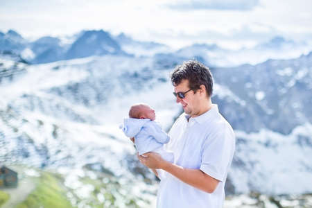 Happy young father playing with his newborn baby in the beautiful snow covered mountains の写真素材