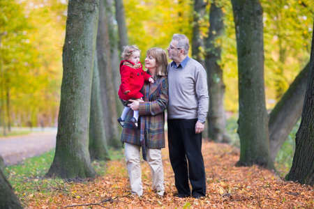 Happy family with a cute toddler girl walking together in a beautiful autumn park with colorful yellow trees の写真素材