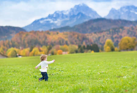Little toddler girl running in a beautiful field between snow covered mountains の写真素材