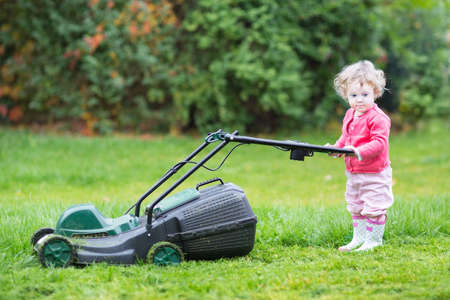 Cute toddler girl with a lawnmower in the garden の写真素材