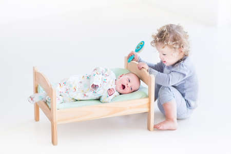 Funny curly toddler girl playing with hew newborn baby brotherの写真素材
