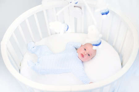 Cute newborn baby boy in a white round crib watching toys の写真素材