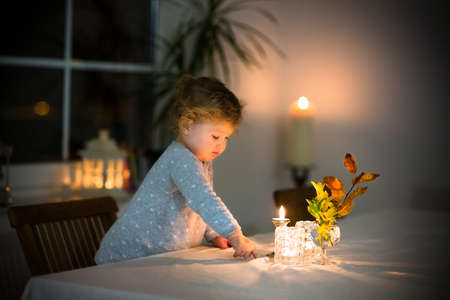 Cute toddler girl watching burning candles in a beautiful dark dining room の写真素材