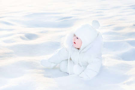 Cute happy baby playing in snow on a sunny winter day の写真素材