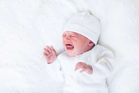 Tiny crying newborn baby ni a white knitted hat and jacket 