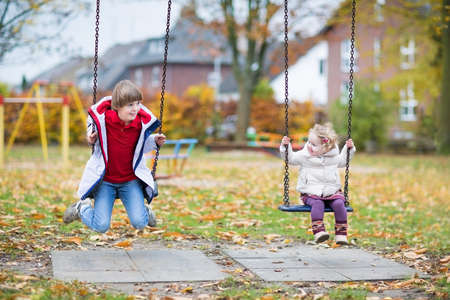 Happy laughing boy and his little baby sister playing together on a swing in autumn の写真素材