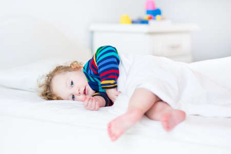Adorable toddler girl waking up in the morning in a sunny white bedroom の写真素材