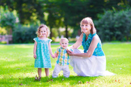 Beautiful young woman playing with two little children, cute curly girl in a summer dress and...