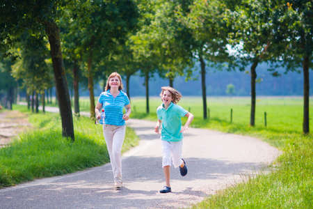 Happy healthy family, active young woman and a funny laughing boy, running together in a beautiful field, enjoying jogging sport outdoors on a sunny summer dayの写真素材