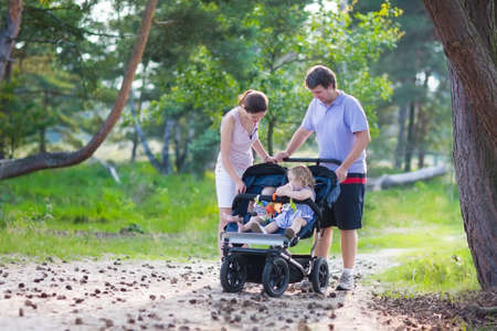Active family, young parents and their two little children, adorable toddler girl and a cute funny baby boy, hiking together in a pine forest pushing an all terrain twin strollerの写真素材