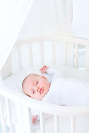 Little newborn baby boy sleeping in a white round crib with canopy  の写真素材