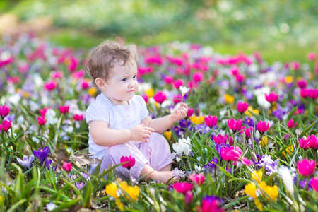 Cute curly little baby sitting between beautiful spring flowers  の写真素材
